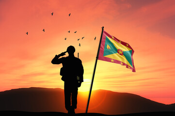 Silhouette of a soldier with the Grenada flag stands against the background of a sunset or sunrise....