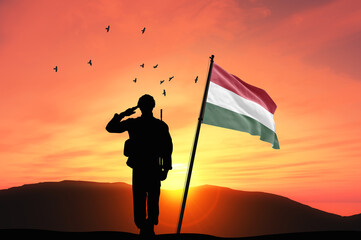 Silhouette of a soldier with the Hungary flag stands against the background of a sunset or sunrise....