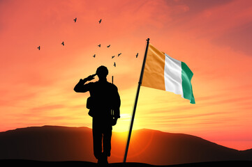 Silhouette of a soldier with the Ivory Coast flag stands against the background of a sunset or...