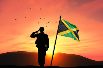 Silhouette of a soldier with the Jamaica flag stands against the background of a sunset or sunrise....