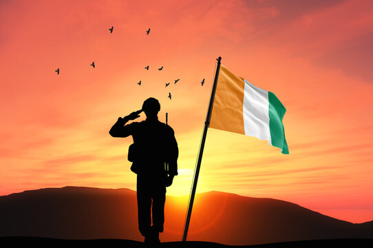 Silhouette of a soldier with the Ivory Coast flag stands against the background of a sunset or sunrise. Concept of national holidays. Commemoration Day.