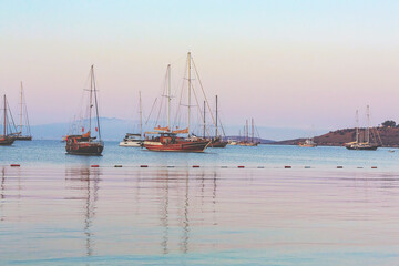 Obraz premium Sailboats at the harbor of Bodrum at first light with pastel tones sky and purple mountains at background. 14 October, 2023. Bodrum, Turkey (Turkiye)