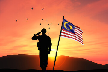 Silhouette of a soldier with the Malaysia flag stands against the background of a sunset or sunrise. Concept of national holidays. Commemoration Day.