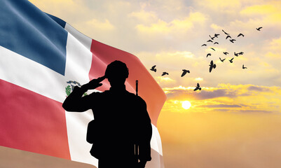 Silhouette of a soldier with the Dominican Republic flag stands against the background of a sunset or sunrise. Concept of national holidays. Commemoration Day. - obrazy, fototapety, plakaty