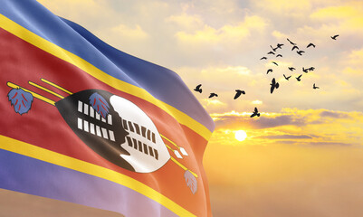 Waving flag of Eswatini against the background of a sunset or sunrise. Eswatini flag for...