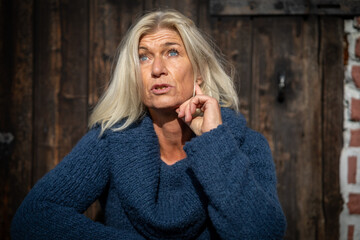 Woman blonde head portraits in her mid-fifties wearing a wide blue knitted sweater, sitting in...