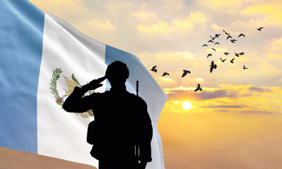 Silhouette of a soldier with the Guatemala flag stands against the background of a sunset or...