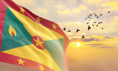 Waving flag of Grenada against the background of a sunset or sunrise. Grenada flag for Independence Day. The symbol of the state on wavy fabric.