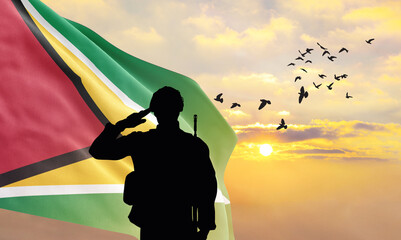 Silhouette of a soldier with the Guyana flag stands against the background of a sunset or sunrise....