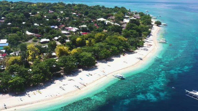 orbital drone shot of island beach in the philippines with boats and local houses 