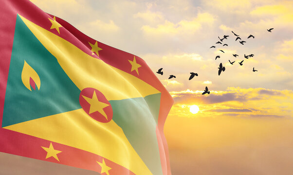 Waving flag of Grenada against the background of a sunset or sunrise. Grenada flag for Independence Day. The symbol of the state on wavy fabric. - Powered by Adobe