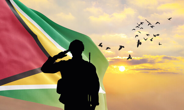 Silhouette of a soldier with the Guyana flag stands against the background of a sunset or sunrise. Concept of national holidays. Commemoration Day.