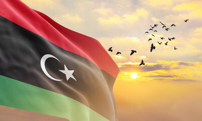Waving flag of Libya against the background of a sunset or sunrise. Libya flag for Independence Day. The symbol of the state on wavy fabric. - obrazy, fototapety, plakaty