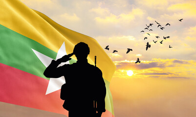 Silhouette of a soldier with the Myanmar flag stands against the background of a sunset or sunrise....