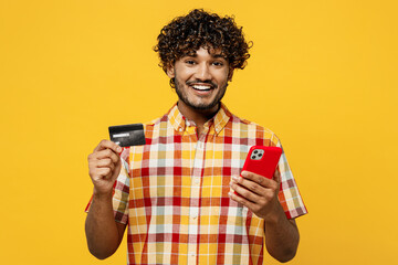 Young Indian man wear shirt casual clothes using mobile cell phone hold credit bank card doing...