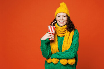 Young smiling happy fun woman she wear green knitted sweater yellow hat scarf hold in hand cup of...
