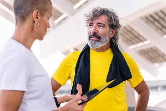 Senior Sports Man Watching Progress Of His Workout On A Tablet And Discussing The Results With His Personal Trainer, Concept Of Healthy And Active Lifestyle