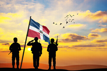 Silhouettes of soldiers with the Dominican Republic flag stand against the background of a sunset or sunrise. Concept of national holidays. Commemoration Day. - obrazy, fototapety, plakaty