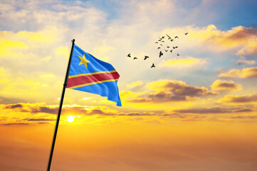 Waving flag of DR Congo against the background of a sunset or sunrise. DR Congo flag for Independence Day. The symbol of the state on wavy fabric.