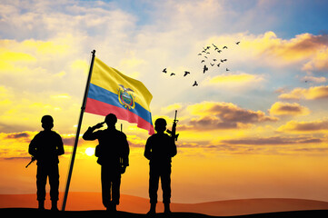 Silhouettes of soldiers with the Ecuador flag stand against the background of a sunset or sunrise....