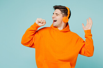 Young happy man he wears orange hoody casual clothes listen to music in headphones sing song in...