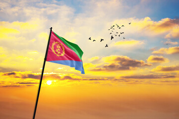 Waving flag of Eritrea against the background of a sunset or sunrise. Eritrea flag for Independence Day. The symbol of the state on wavy fabric.