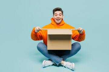 Full body surprised young man he wearing orange hoody casual clothes sitting hold unpacking...