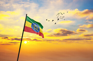 Waving flag of Ethiopia against the background of a sunset or sunrise. Ethiopia flag for Independence Day. The symbol of the state on wavy fabric.