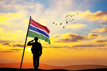 Silhouette of a soldier with the Gambia flag stands against the background of a sunset or sunrise. Concept of national holidays. Commemoration Day.