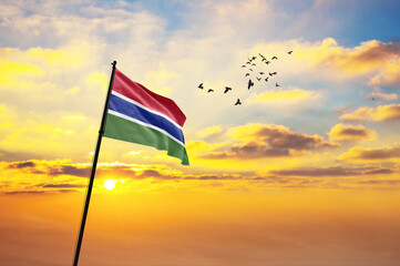 Waving flag of Gambia against the background of a sunset or sunrise. Gambia flag for Independence Day. The symbol of the state on wavy fabric.