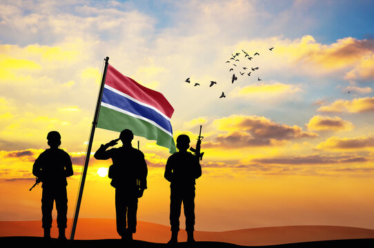 Silhouettes of soldiers with the Gambia flag stand against the background of a sunset or sunrise. Concept of national holidays. Commemoration Day.