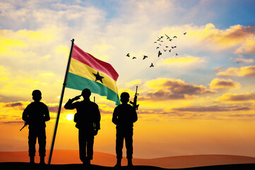 Silhouettes of soldiers with the Ghana flag stand against the background of a sunset or sunrise....