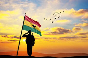 Silhouette of a soldier with the Ghana flag stands against the background of a sunset or sunrise....