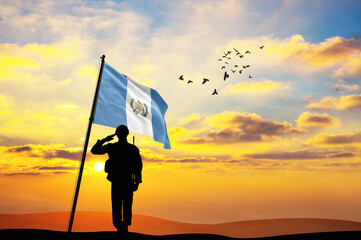 Silhouette of a soldier with the Guatemala flag stands against the background of a sunset or...