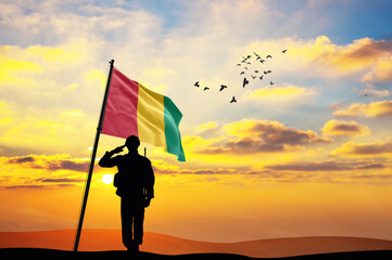 Silhouette of a soldier with the Guinea flag stands against the background of a sunset or sunrise. Concept of national holidays. Commemoration Day.
