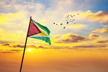 Waving flag of Guyana against the background of a sunset or sunrise. Guyana flag for Independence Day. The symbol of the state on wavy fabric.