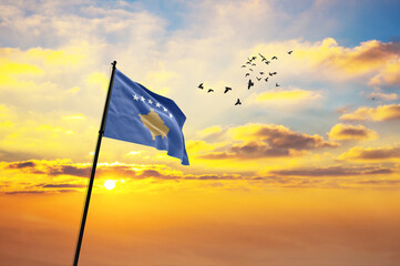 Waving flag of Kosovo against the background of a sunset or sunrise. Kosovo flag for Independence Day. The symbol of the state on wavy fabric.