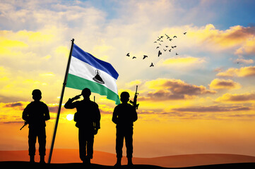 Silhouettes of soldiers with the Lesotho flag stand against the background of a sunset or sunrise. Concept of national holidays. Commemoration Day.