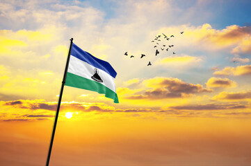 Waving flag of Lesotho against the background of a sunset or sunrise. Lesotho flag for Independence Day. The symbol of the state on wavy fabric.