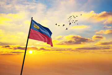 Waving flag of Liechtenstein against the background of a sunset or sunrise. Liechtenstein flag for Independence Day. The symbol of the state on wavy fabric.