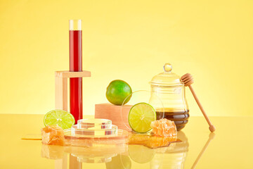 Honey is filled into a test tube, glass platforms, fresh lemons and raw beeswax are displayed on a yellow background. Lemon and honey are a healthy duo of ingredients.