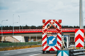 A road works sign with a flashing arrow directs traffic to the different lane on a highway. A...