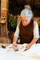 Senior woman checking with hand during flower pounding on fabric near hammer in workshop