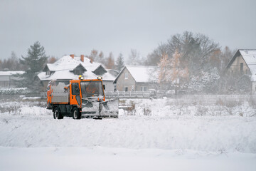 An orange truck with a salt and sand spreader clears the snow and ice from the road. The winter...