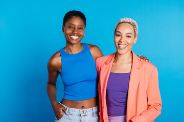 Portrait of a smiling young female couple in front of a blue background at studio. Two women together at studio.