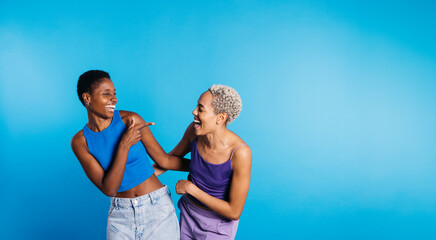 Two young cheerful women dancing in a studio with a blue background.