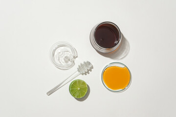 Honey is served in glass containers and half a lemon is displayed on a white background. Natural ingredients to make tea to support health. Top view.