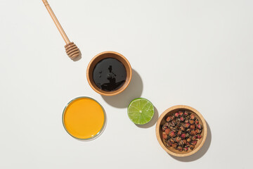 On a white background, wooden bowls cradle honey and dried rose buds, with a halved fresh lemon and honey drizzle. Conveying a healthcare concept with natural ingredients.