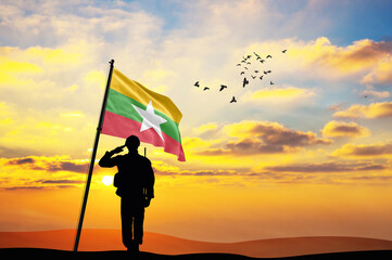 Silhouette of a soldier with the Myanmar flag stands against the background of a sunset or sunrise....