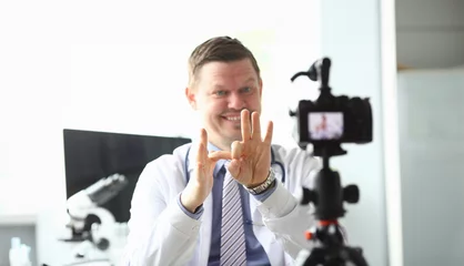 Fotobehang Focus on male hands of handsome doctor showing funny jokes with gestures by hands. Smiling blogger recording popular video content to camera. Blogging concept © H_Ko